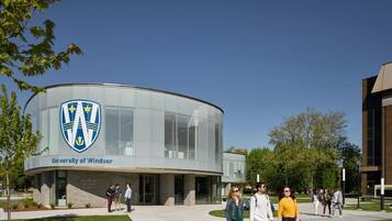 Een modern gebouw met een glazen gevel en een logo bij de ingang, omringd door een gazon en enkele mensen die lopen.