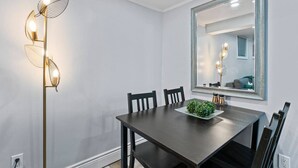 A dining area with a dark wooden table, four chairs, a decorative floor lamp, a mirror, and a small plant on the table.