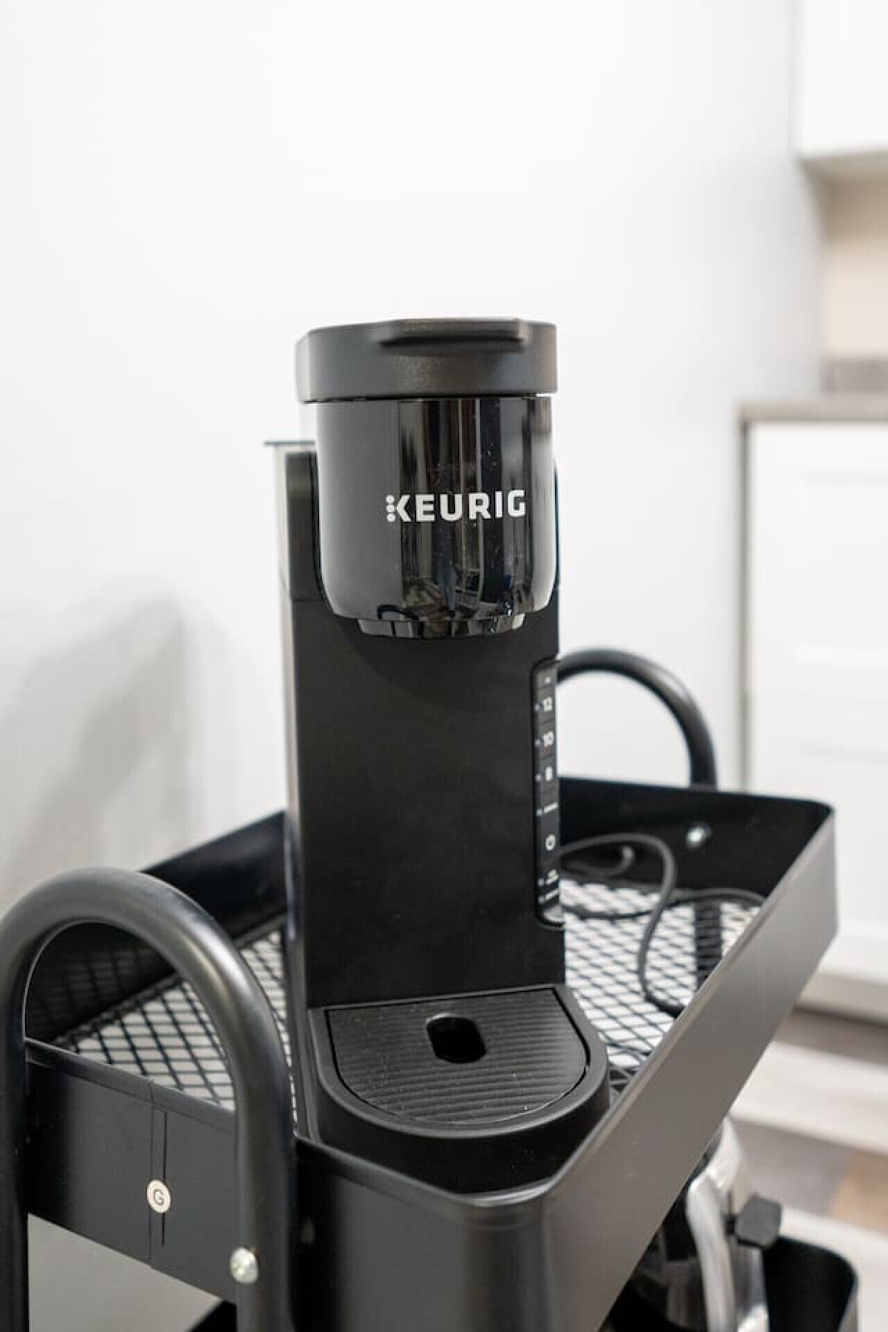 Une machine à café Keurig noire, posée sur un support métallique noir, avec un plateau.