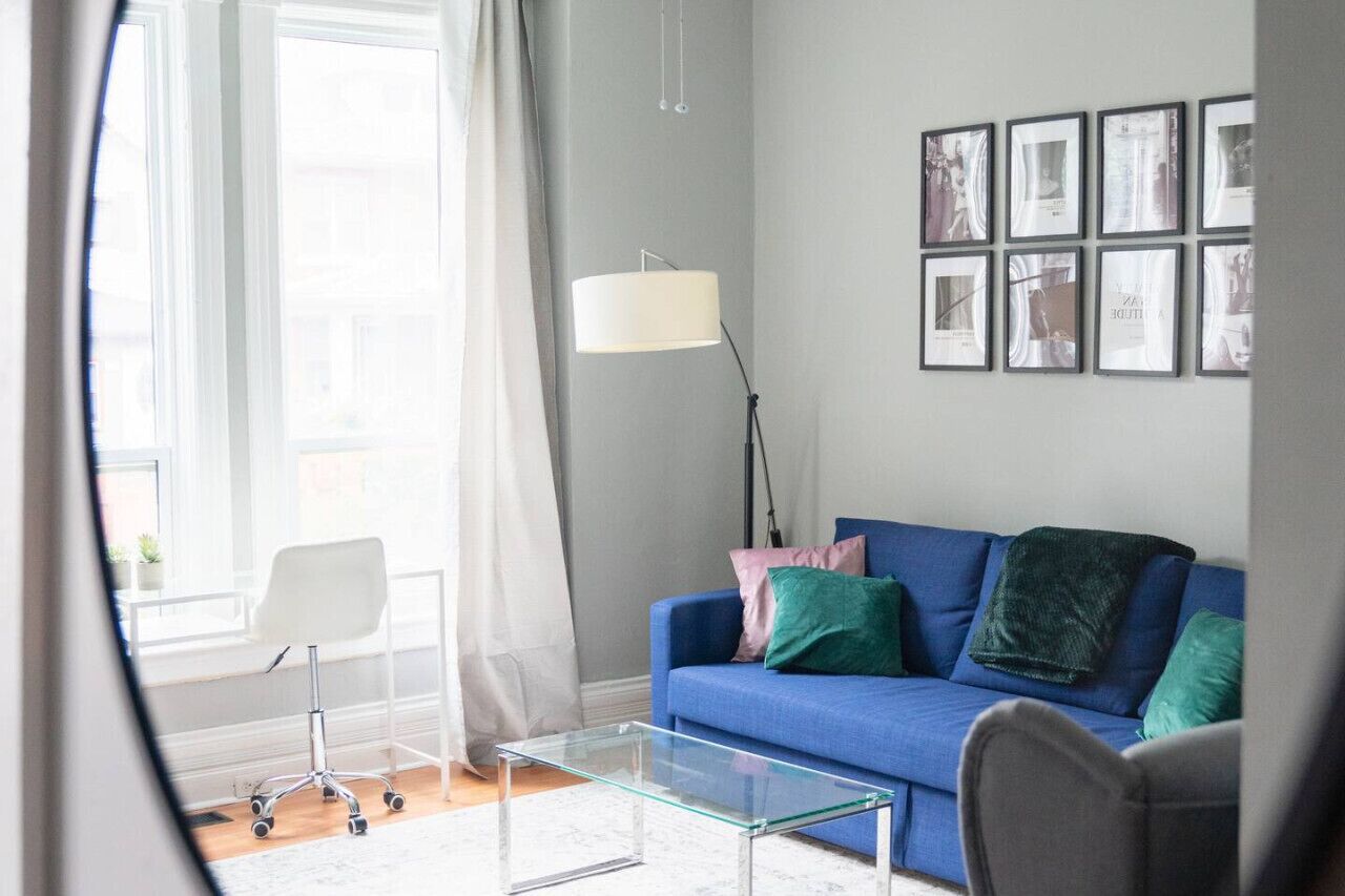 Un salon moderne avec un canapé bleu, une table basse en verre, un fauteuil de bureau blanc et une lampe sur pied.