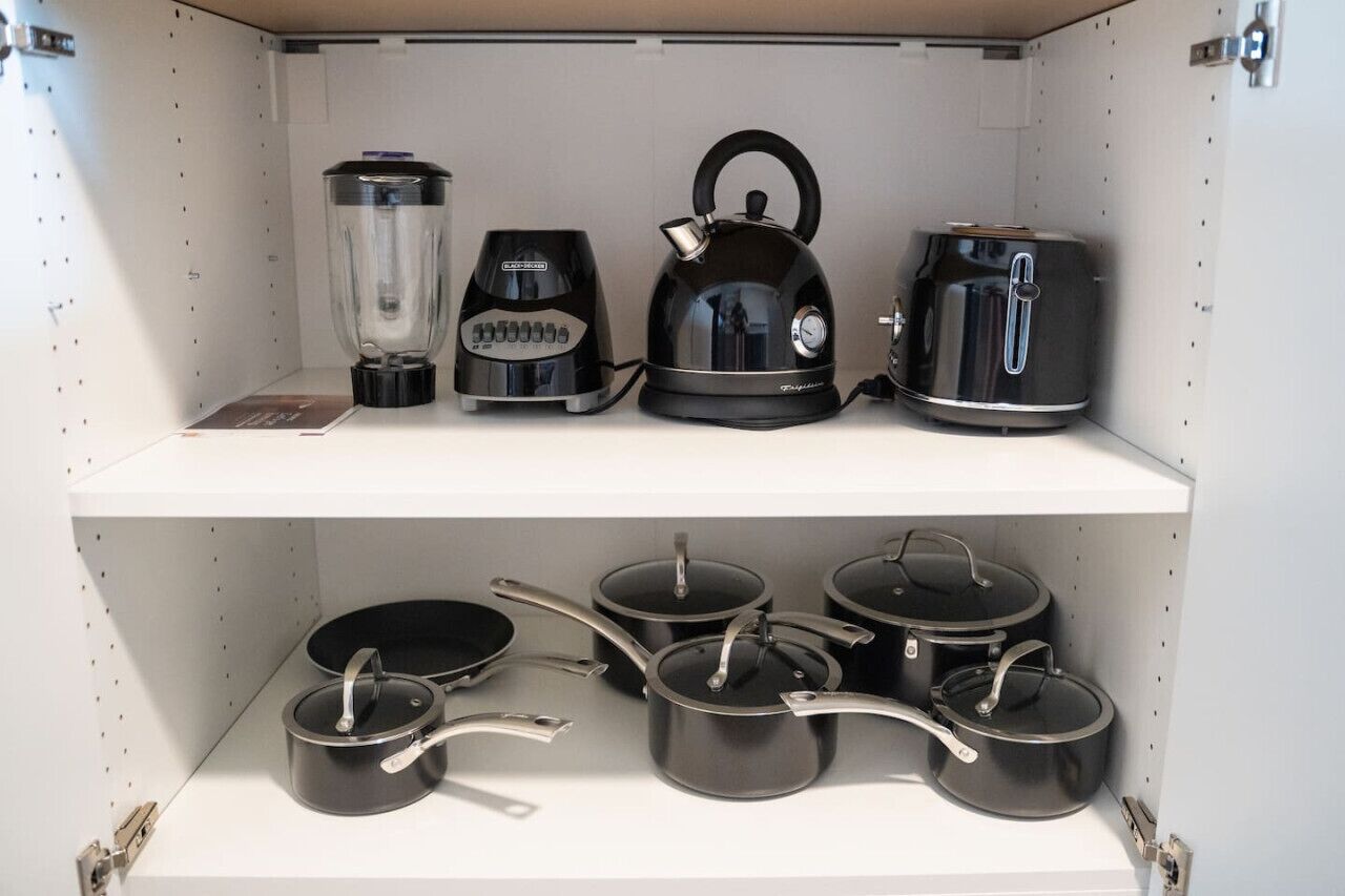 Une étagère de cuisine avec un mixeur, une bouilloire et un grille-pain, et en dessous, plusieurs casseroles et poêles.