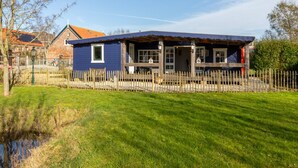 Une maison bleue avec une clôture en bois, une cour verdoyante et un étang.