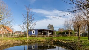 Une maison avec un étang devant, entourée d’arbres et d’une clôture.
