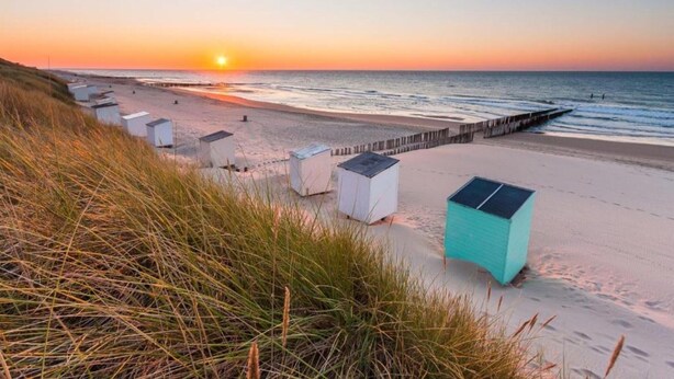Une plage avec plusieurs petits cabanons blancs et une jetée en bois qui s’avance dans l’eau.