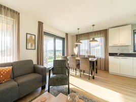 Una sala de estar moderna con sofá, sillas, una mesa de comedor y una cocina con armarios blancos y encimera negra.