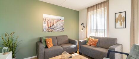 A living room with two grey sofas, a wooden coffee table, a floor lamp, and a beach-themed painting on the wall.