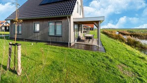 A modern house with a sloped roof, large windows, and a covered outdoor area with a table and chairs. - Holiday Home in Scherpenisse Near Nature Reserve (Scherpenisse)