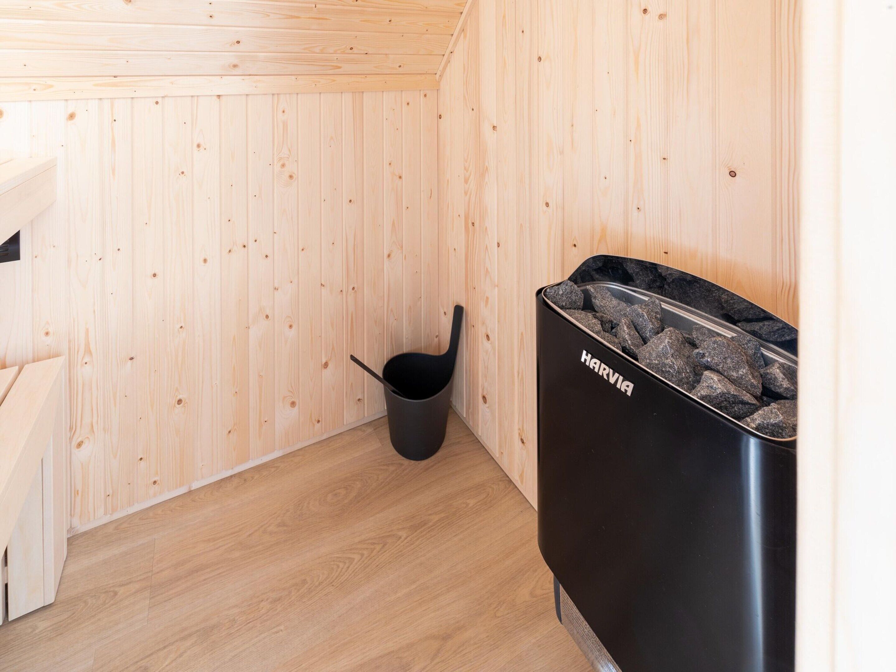 A wooden interior with a black trash bin labeled "HARVIA" and a black bucket.