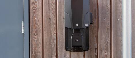 Una unidad exterior negra fijada a una pared de madera, probablemente para calefacción o aire acondicionado.
