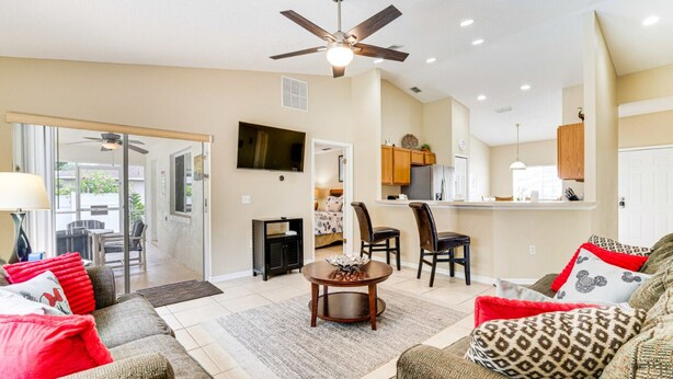 A spacious living room with a ceiling fan, a dining area with chairs, and a kitchen with cabinets. - FREE Disney Plus & Hulu ~ 4 BR/2 BA Heated Pool Home 9mi to Disney Theme Parks (Davenport)