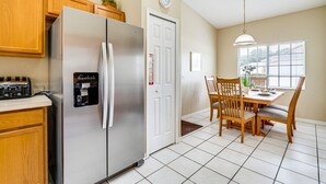 A kitchen with a stainless steel refrigerator, wooden cabinets, a built-in coffee maker, and a dining area with a table and chairs. - FREE Disney Plus & Hulu ~ 4 BR/2 BA Heated Pool Home 9mi to Disney Theme Parks (Davenport)
