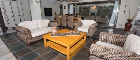 A spacious living area with a large wooden coffee table, patterned sofas, and a stone-tiled floor.