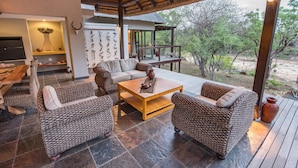 An outdoor living area with wicker furniture, a wooden coffee table, and a thatched roof structure. - Luxury Villa With a Swimming Pool in Hoedspruit (Hoedspruit)