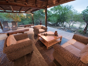 An outdoor patio with wicker furniture, a wooden table, and a view of the surrounding trees. - Luxury Villa With a Swimming Pool in Hoedspruit (Hoedspruit)