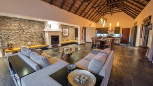 A spacious living area with a stone wall, a glass coffee table, and a fireplace. - Luxury Villa With a Swimming Pool in Hoedspruit (Hoedspruit)