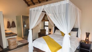 A four-poster bed with a canopy, a bedside table, a nightstand, a wicker basket, and a bathroom with a sink and towel rack. - Luxury Villa With a Swimming Pool in Hoedspruit (Hoedspruit)