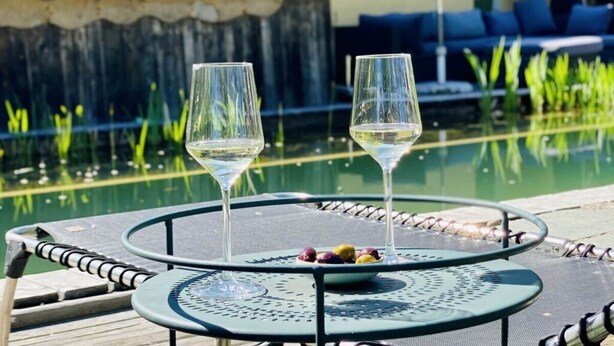 Een tafel met twee wijnglazen en een schaal olijven bij een zwembad.