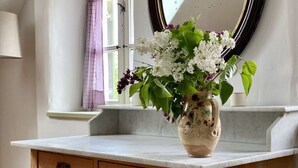 Een badkamer met een houten wastafel, een vaas met bloemen, een raam met uitzicht en een spiegel.
