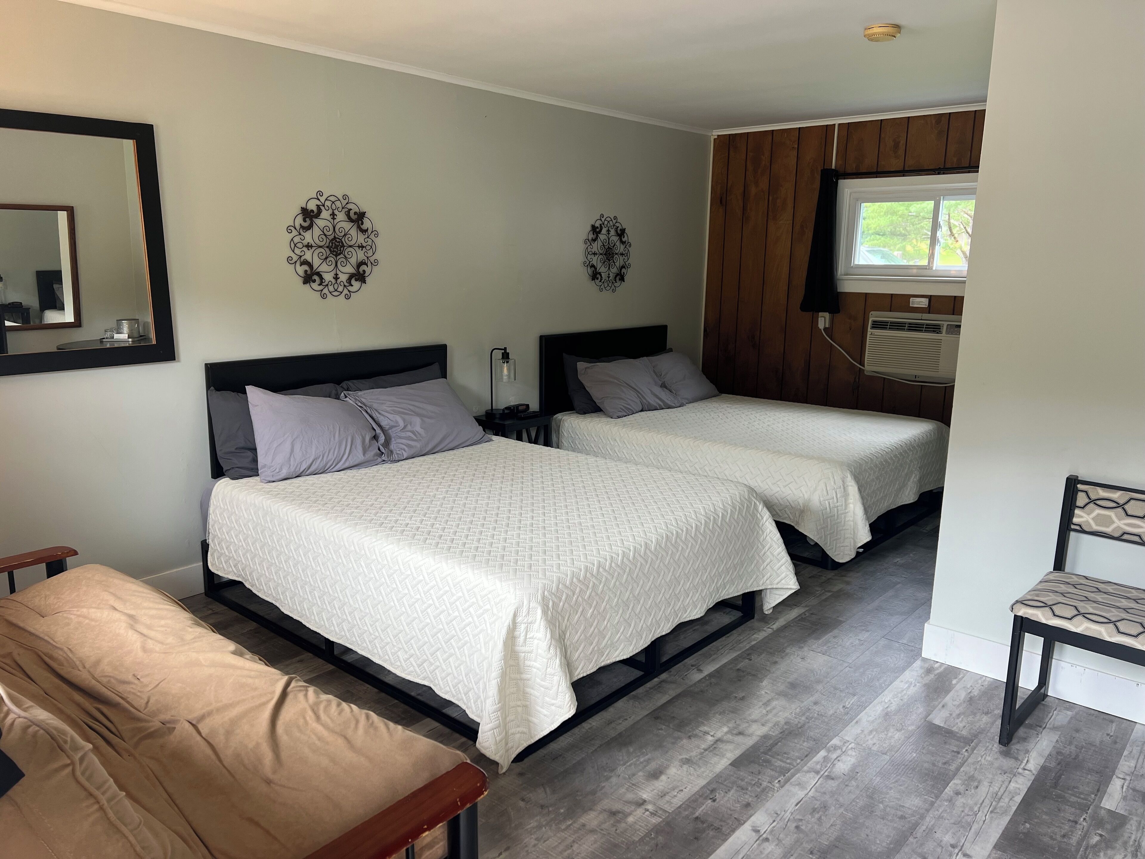 Une chambre avec deux lits, un banc, un miroir, des éléments décoratifs muraux et un appareil de climatisation.