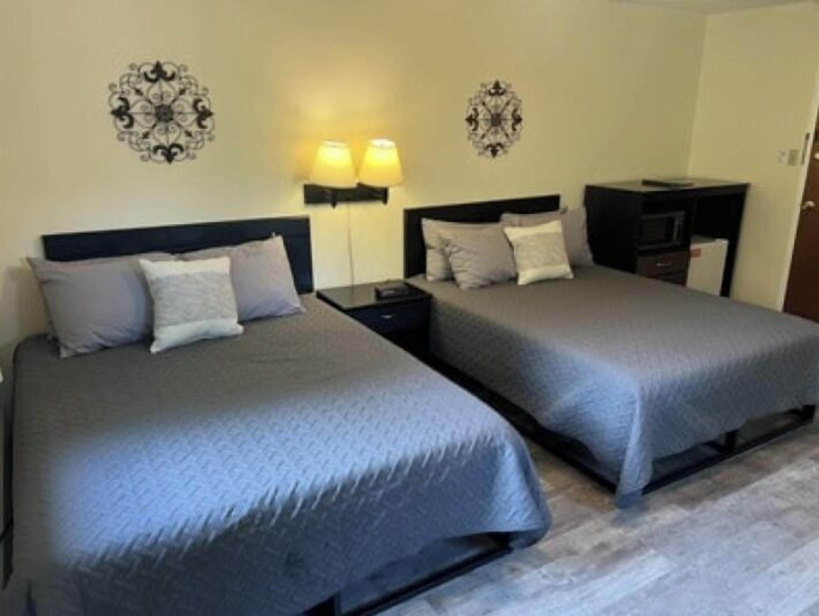 A hotel room with two single beds, each with a headboard and bedside tables. There are wall-mounted lamps on either side of the beds.