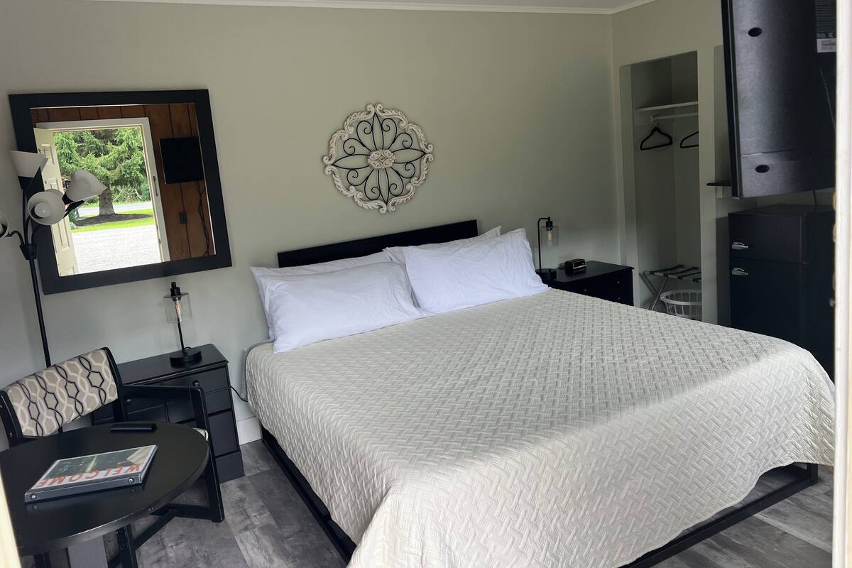 A neatly arranged bedroom with a bed, bedside tables, a chair, a mirror, and a decorative wall piece.