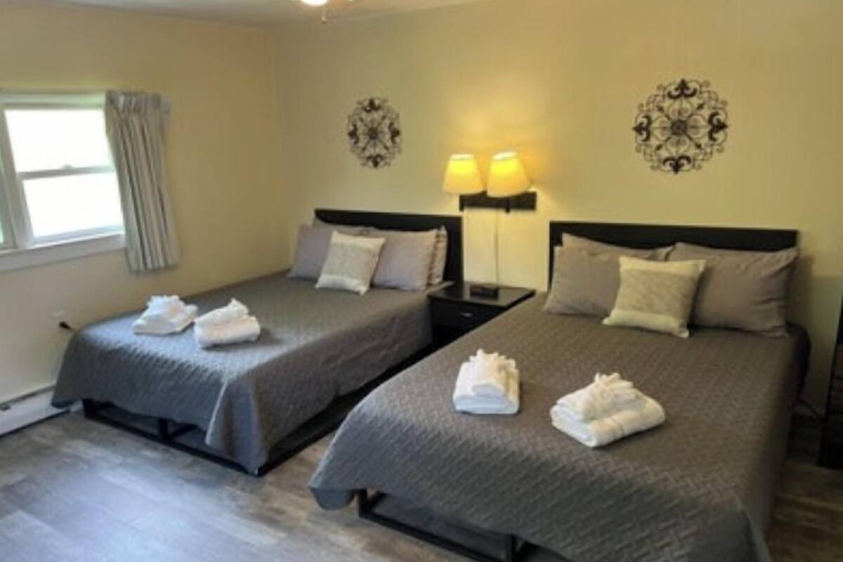 A hotel room with two beds, each with a neatly folded towel, a nightstand with a lamp, and decorative wall art.