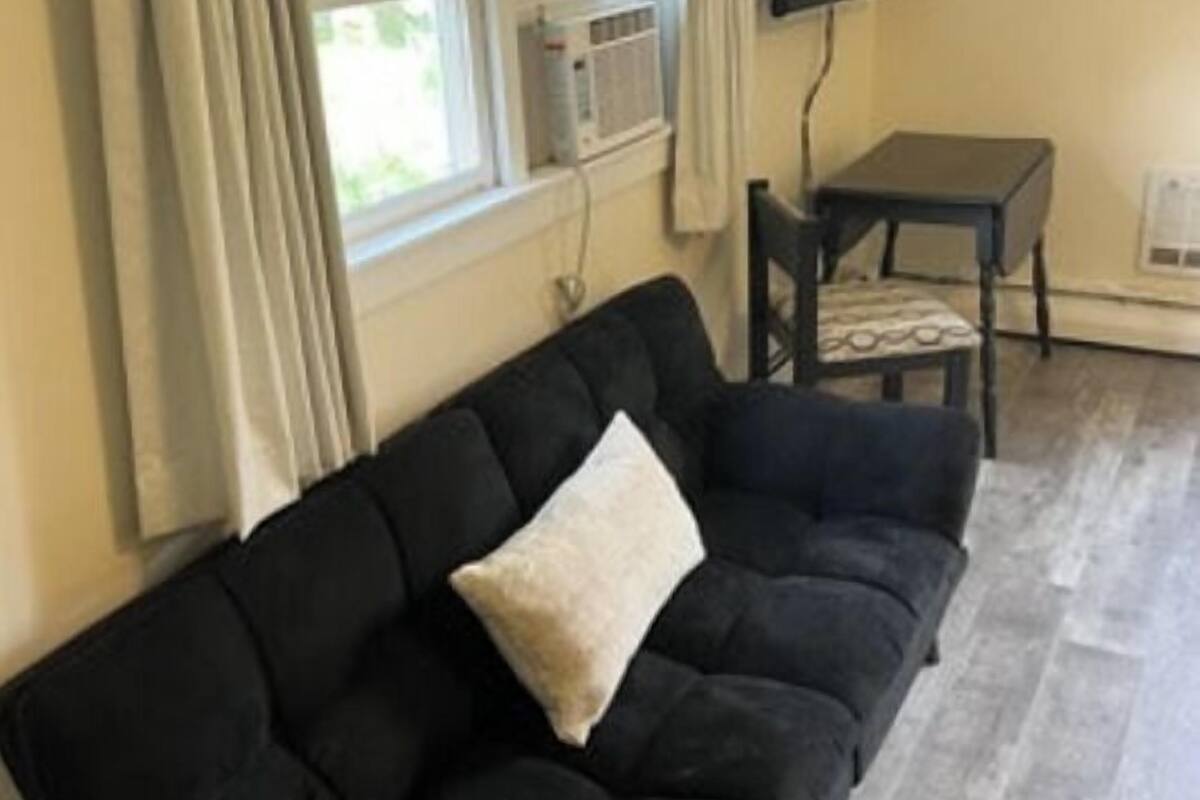 A living room with a black sofa, a small table, a TV, and a window with curtains.