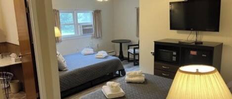 A hotel room with two beds, a TV, a desk, and a lamp.