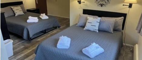 Habitación de hotel con dos camas, cada una con cubrecama gris y toallas blancas. Hay lámparas de pared a ambos lados de las camas.