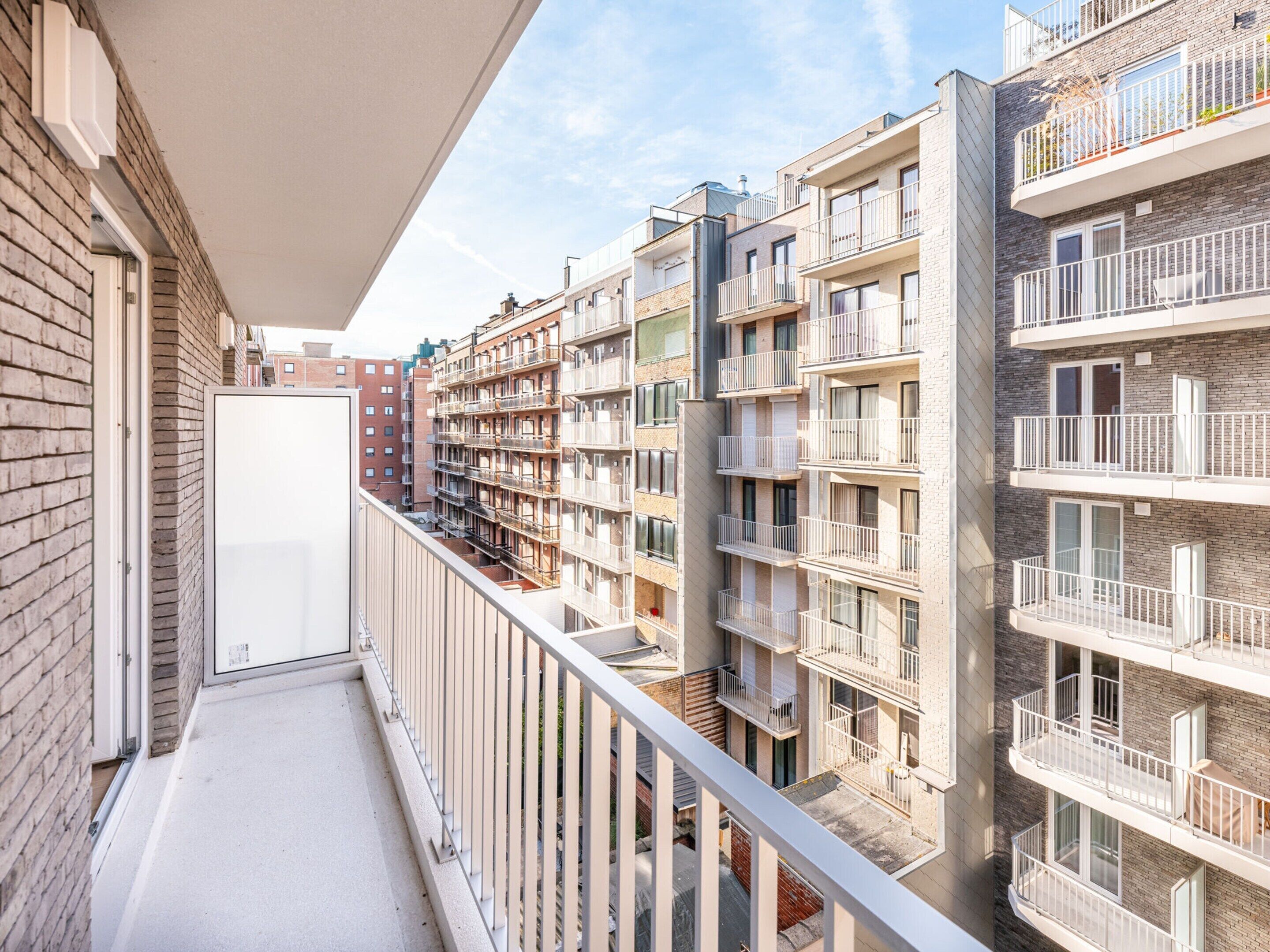 Um edifício residencial com vários andares, varandas, fachadas de tijolo e céu claro.