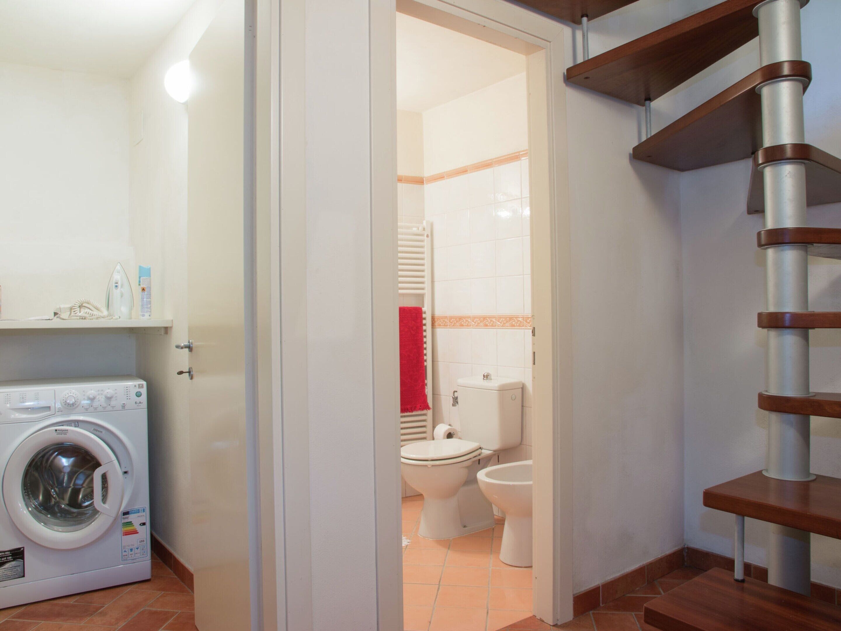A laundry area with a washing machine, a bathroom with a toilet and sink, and a wooden staircase.