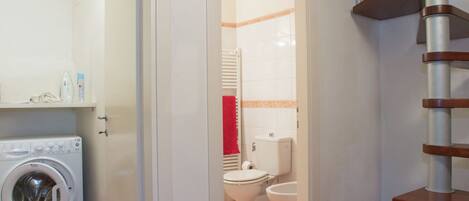 A laundry area with a washing machine, a bathroom with a toilet and sink, and a wooden staircase.