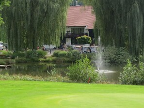 A serene lakeside setting with a house featuring a red-tiled roof and a balcony overlooking the water. - Weiherhof Comfortable Holiday Residence (Wadern)
