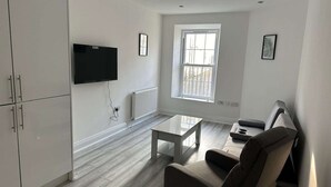 Una sala de estar moderna con un televisor de pantalla plana, un sofá, una mesa de centro y un ventanal con persianas.