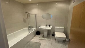 A modern bathroom with a bathtub, a sink, a toilet, and a mirror. - Immaculate 1-bed Apartment in Walton on the Naze (Walton on the Naze)