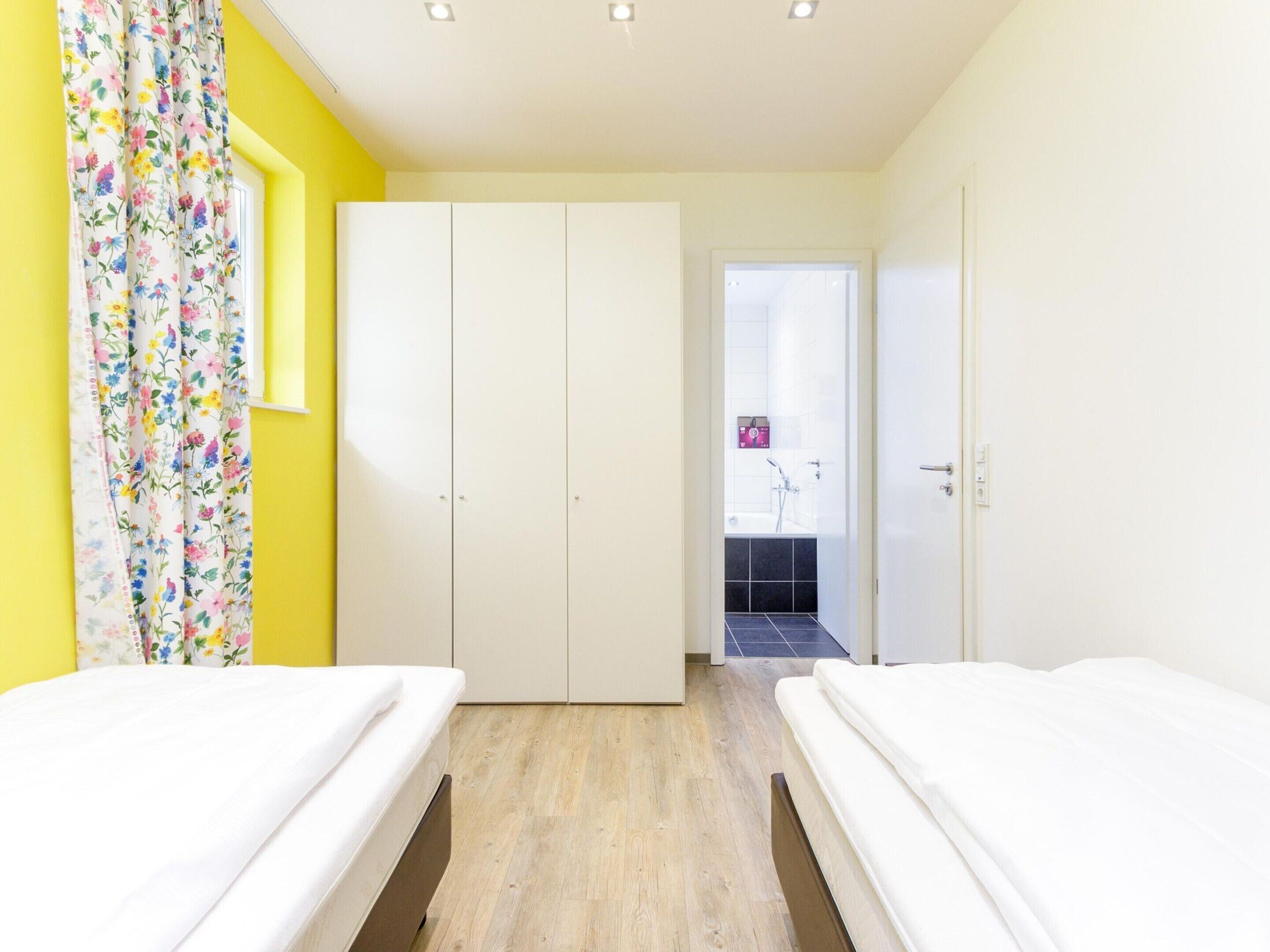 Een slaapkamer met twee bedden, een kledingkast en een badkamer die door een open deur zichtbaar is.