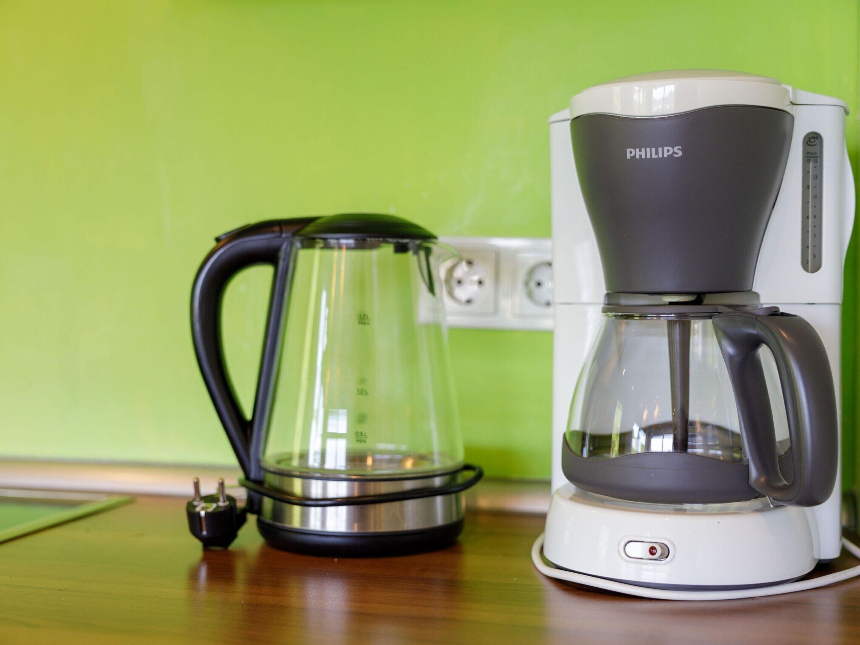 Eine Kaffeemaschine und eine Glaskaraffe auf einem Holztisch vor einer grünen Wand.