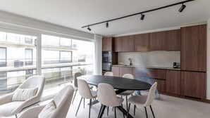 A modern kitchen with wooden cabinets, a black countertop, and a round dining table with chairs. - Stylish Stay in De Haan (De Haan)