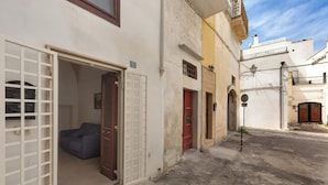 A narrow street with buildings on either side, featuring a door with a metal gate, a red door, and a small balcony with a railing. - 3910 Casa Nanà by Barbarhouse (Nardò)