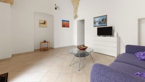 A spacious living room with a glass table, a sofa, and a TV on a white cabinet. - 3910 Casa Nanà by Barbarhouse (Nardò)