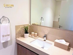 Een badkamer met een wastafel, spiegel, handdoekrek, een potplant en toiletartikelen.