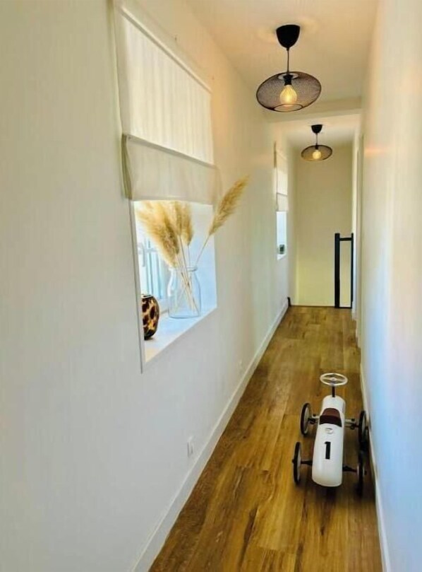 A hallway with wooden flooring, a white wall, and a ceiling light fixture.