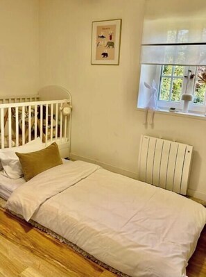 Ein Schlafzimmer mit einem Einzelbett, einem Babybett, einem Heizkörper und einem Fenster mit Blick ins Grüne.