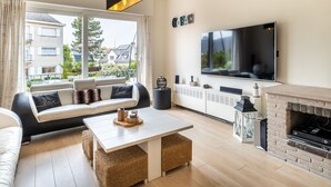 A modern living room with a sofa, a coffee table, a fireplace, a TV, and a view of the outside. - Villa Near Sea and Shops in Belgium (Koksijde)