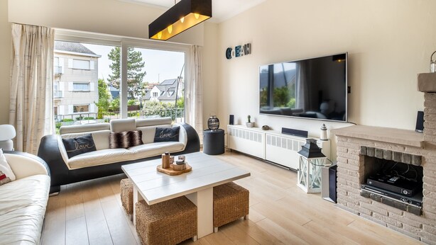 A modern living room with a sofa, a coffee table, a fireplace, a TV, and a large window with curtains. - Villa Near Sea and Shops in Belgium (Koksijde)