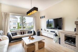 Ein modernes Wohnzimmer mit einer Couch, einem Couchtisch, einem Kamin, einem Fernseher und einem großen Fenster mit Vorhängen.