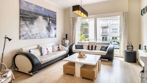 A modern living room with a large ocean painting, a black leather sofa, a white coffee table, and a wicker ottoman. - Villa Near Sea and Shops in Belgium (Koksijde)