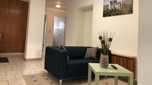 A living room with a dark blue sofa, a small table with a vase, and a painting of a castle on the wall. - Family Apartment Bavaria (Fuessen)
