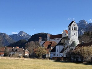 A church with a bell tower and a clock, surrounded by houses and mountains.