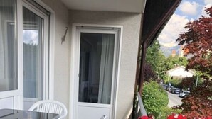 A balcony with a table and chairs, a potted plant with flowers, and a view of a street and buildings. - Family Apartment Bavaria (Fuessen)